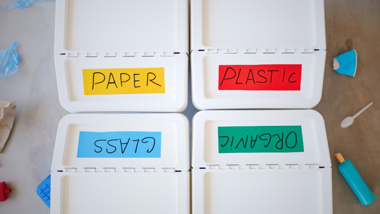 Quattro cassonetti bianchi per la raccolta differenziata in condominio, etichettati con i colori e le scritte: Paper, Plastic, Glass, Organic.
