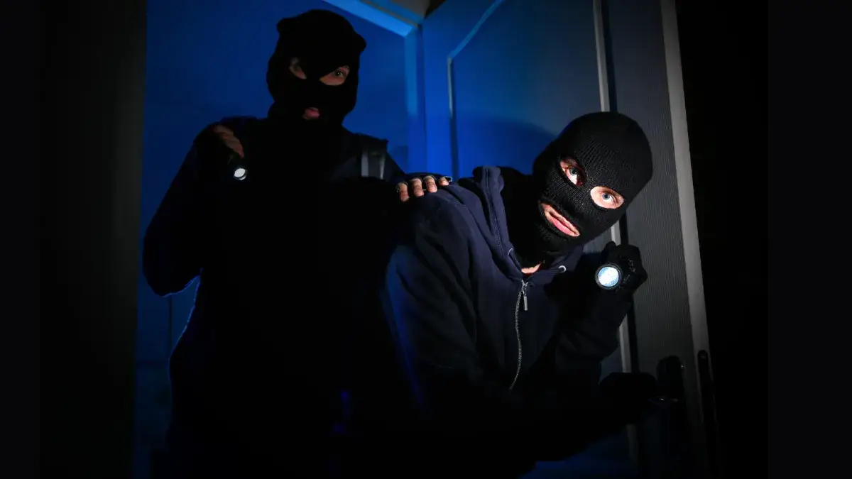 Due ladri incappucciati entrano di notte in un'abitazione condominiale forzando una porta, simbolo dei furti in condominio e della necessità di rafforzare la sicurezza domestica.