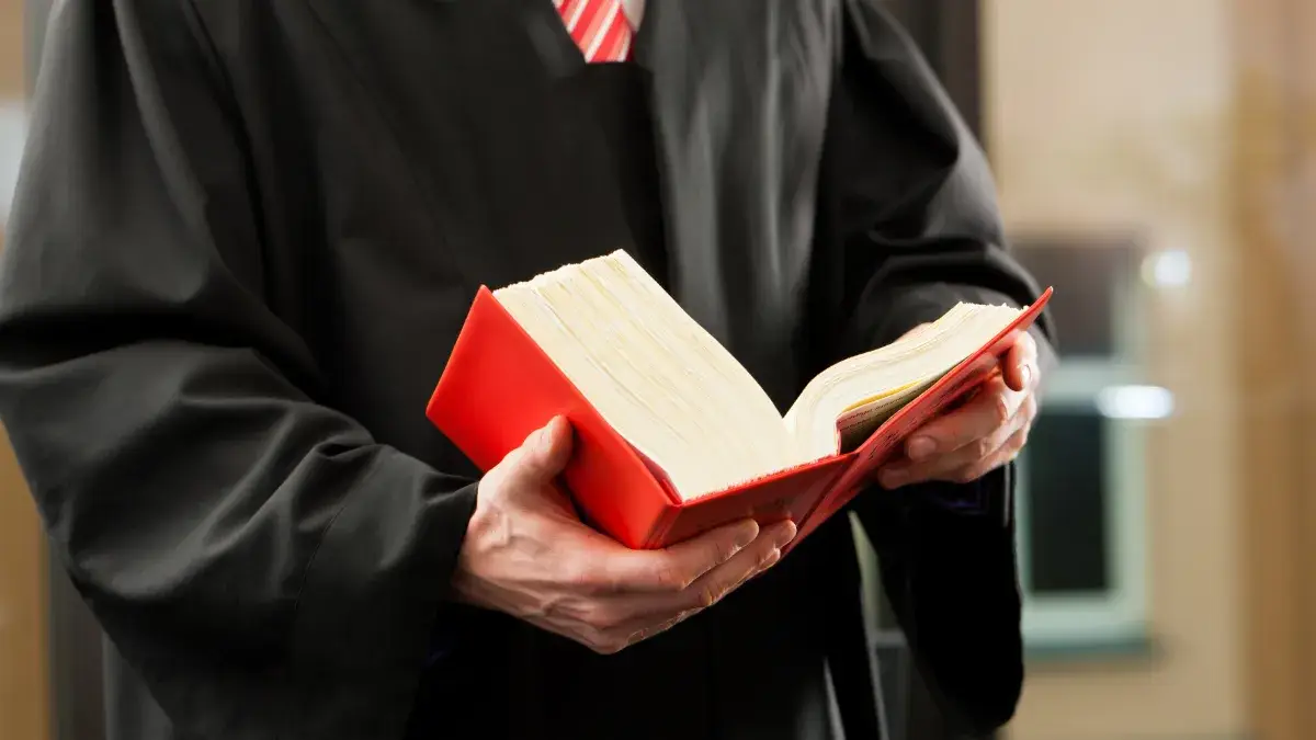 Giudice in toga nera tiene in mano un codice civile rosso aperto, simbolo della normativa che regola il condominio secondo gli articoli del codice civile italiano.